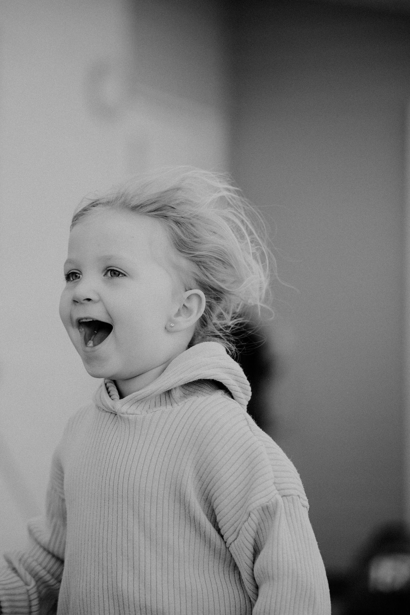 A black and white portrait captures pure joy and laughter with windblown hair and a cozy sweater.