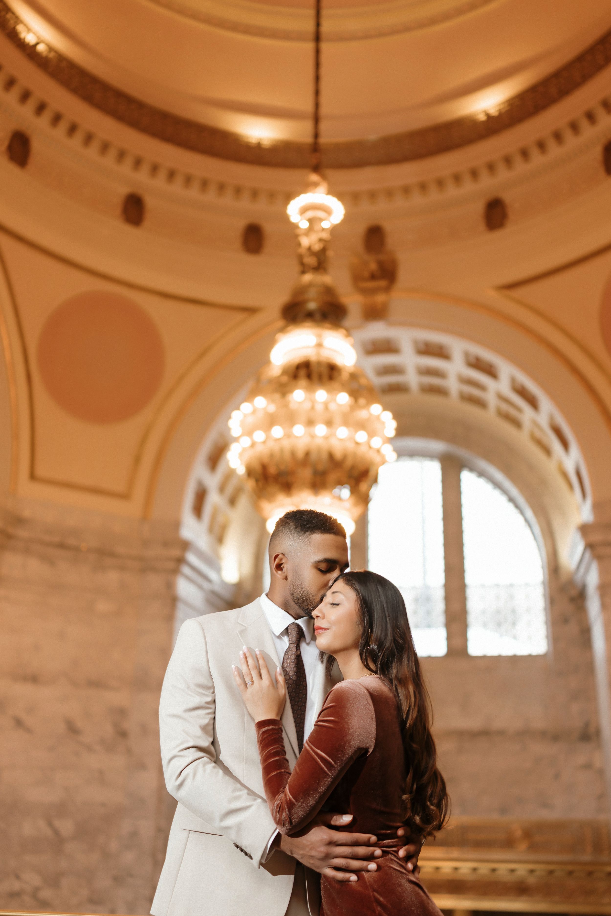 Romantic couple shares intimate moments in an ornate historic building with domed ceiling and elegant architecture.