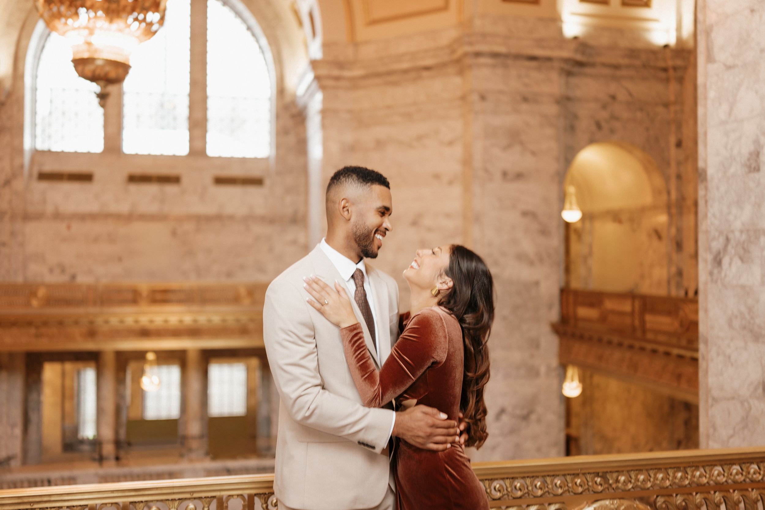 Couple shares intimate moments in a grand historic building with ornate architectural details and warm lighting.
