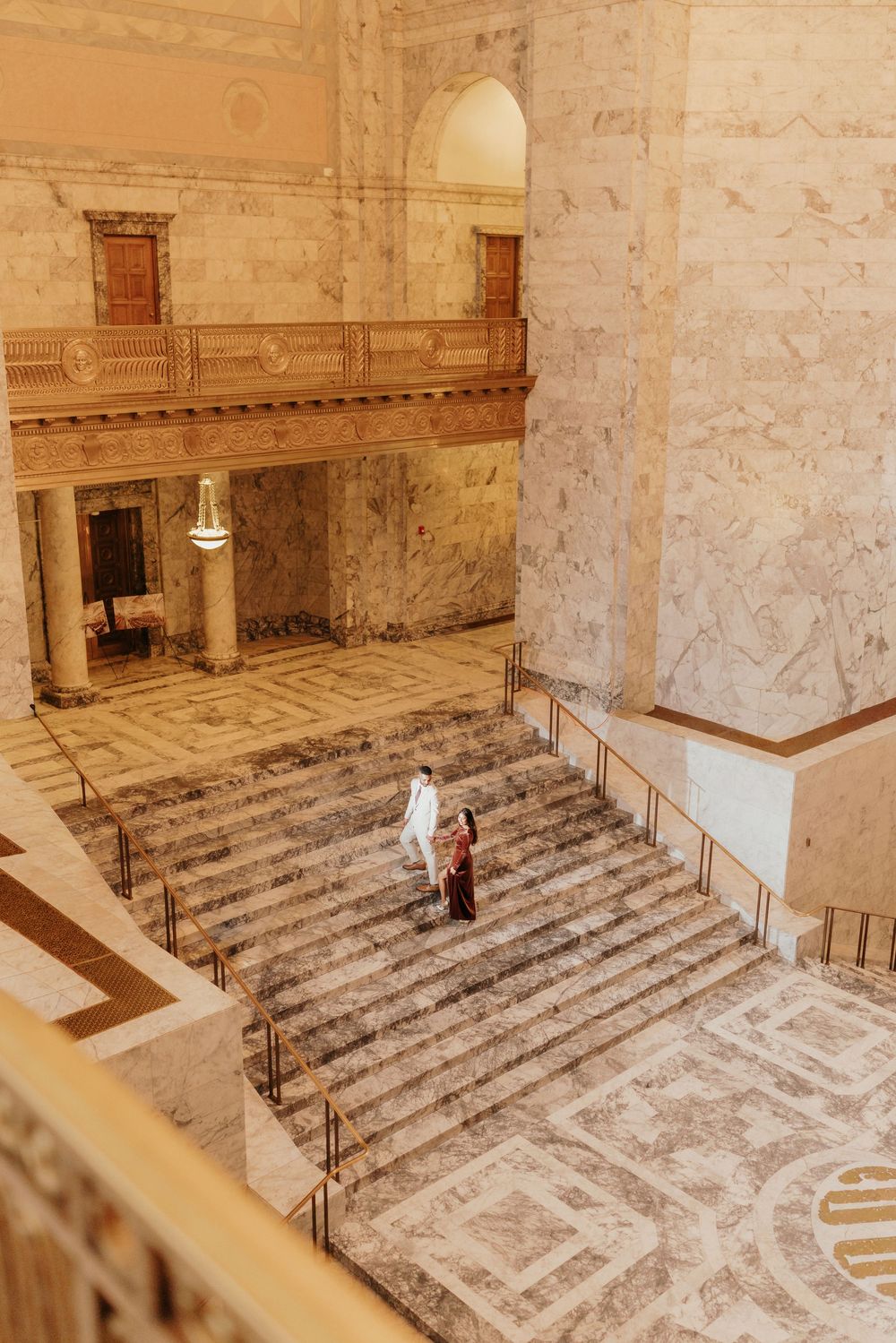 A person in white stands on ornate marble steps inside a grand historic building with classical architectural details.