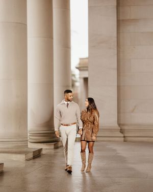 Couple walking through elegant colonnade with tall white pillars creating a dramatic architectural perspective.
