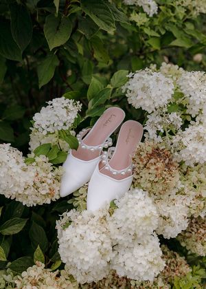 White bridal shoes displayed among blooming hydrangea flowers in a garden setting.