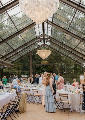 Elegant wedding reception setup in a glass conservatory with crystal chandeliers and long dining tables.