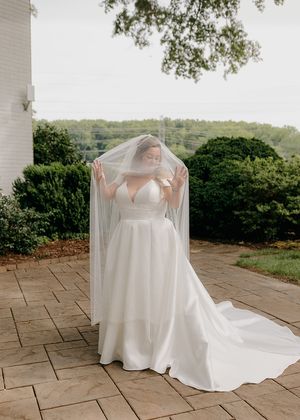 Bride in flowing white dress and veil posing on stone patio with mountain view.
