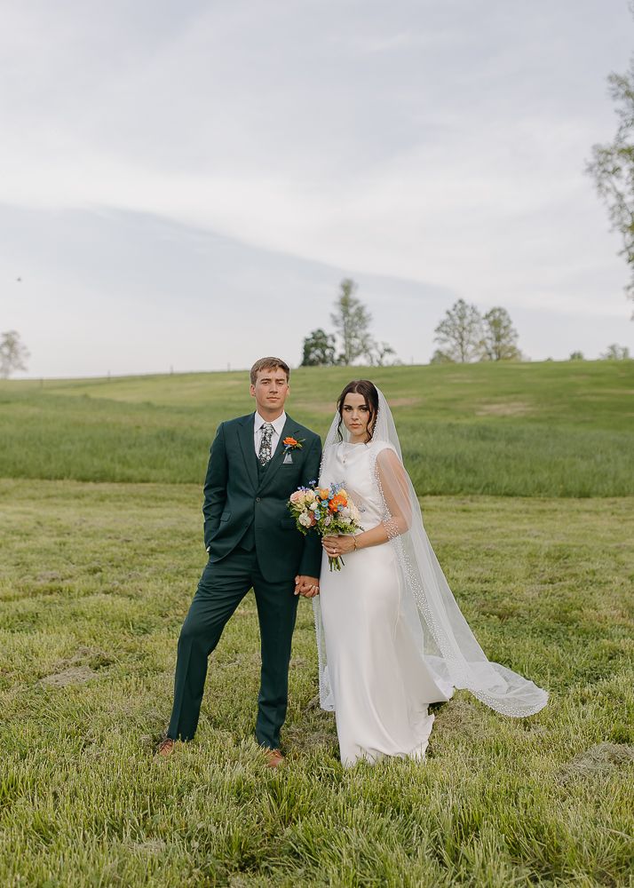 Newlyweds pose together on a grassy hillside in a romantic outdoor wedding portrait.