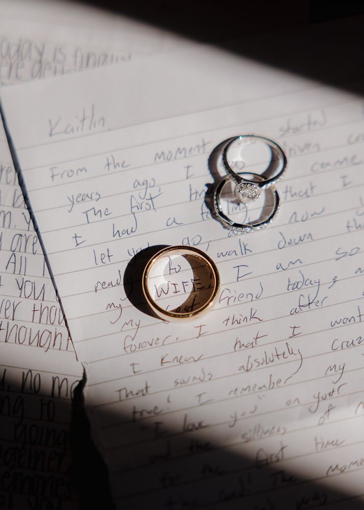 Wedding rings casting shadows on handwritten vows or love letters.