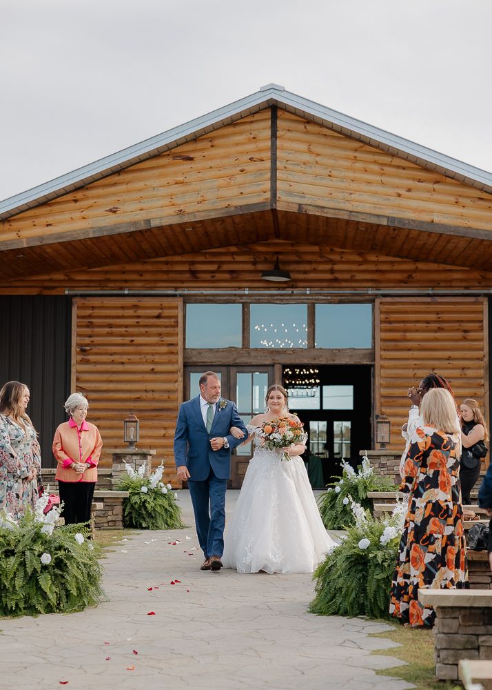 Wedding ceremony outside rustic log cabin venue with floral decorations.