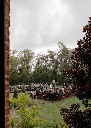 Wide view of outdoor wedding ceremony with rows of wooden chairs on grassy lawn.