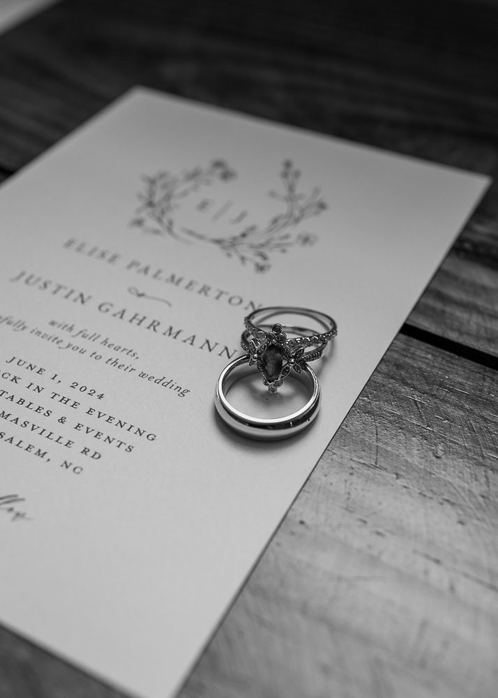 Wedding invitation suite with elegant typography and wedding rings arranged on dark wood surface.