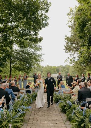 Outdoor wedding ceremony on stone patio surrounded by lush greenery and trees.