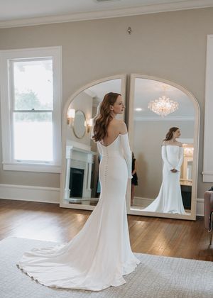 Flowing white wedding dress with train photographed in elegant room with arched mirrors.
