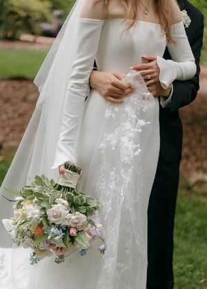 Close-up of elegant white wedding dress and pastel floral bouquet.