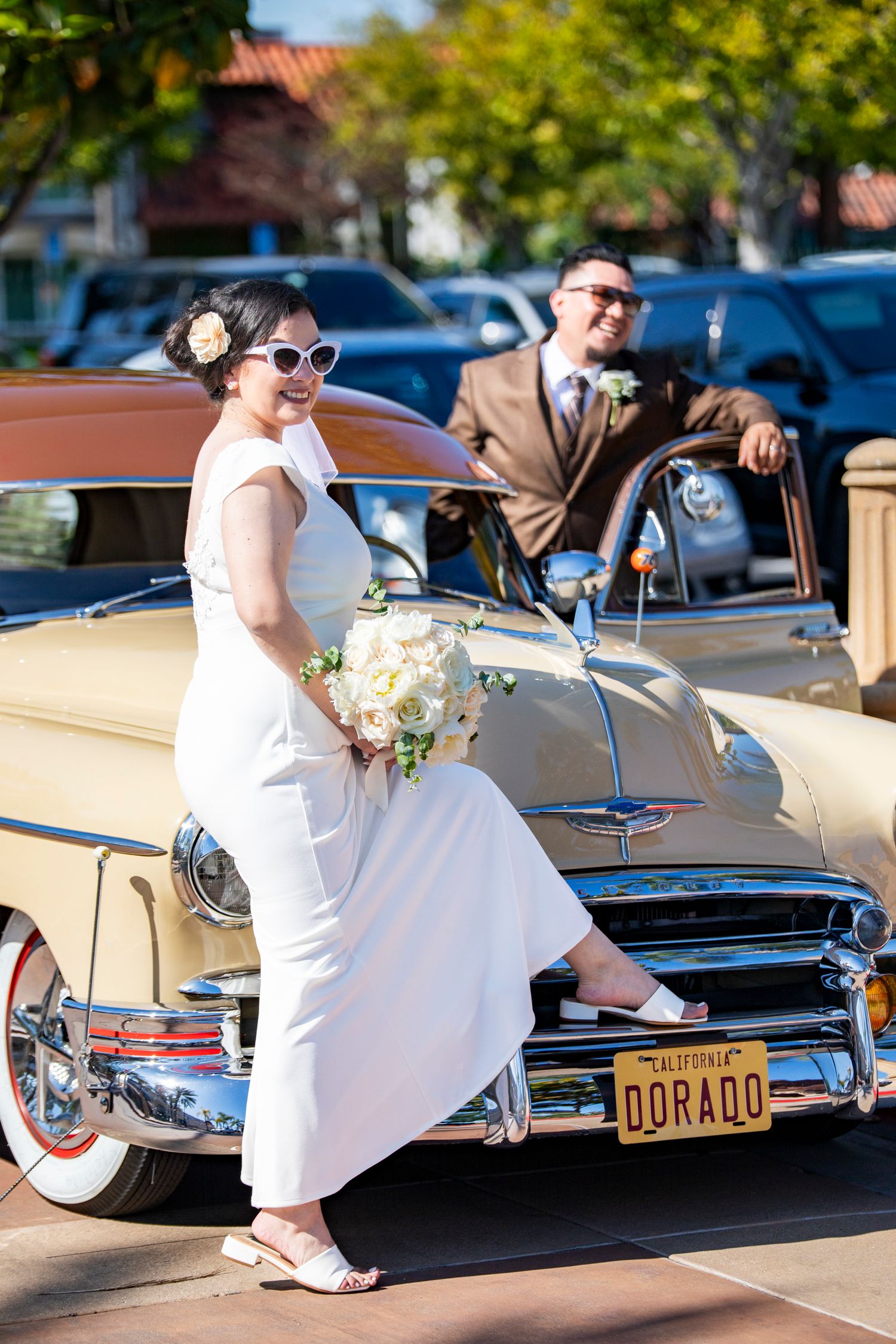 Outside the Laguna Hills Civic Center, bride and groom in retro style pose together in front of a vintage yellow classic car.
