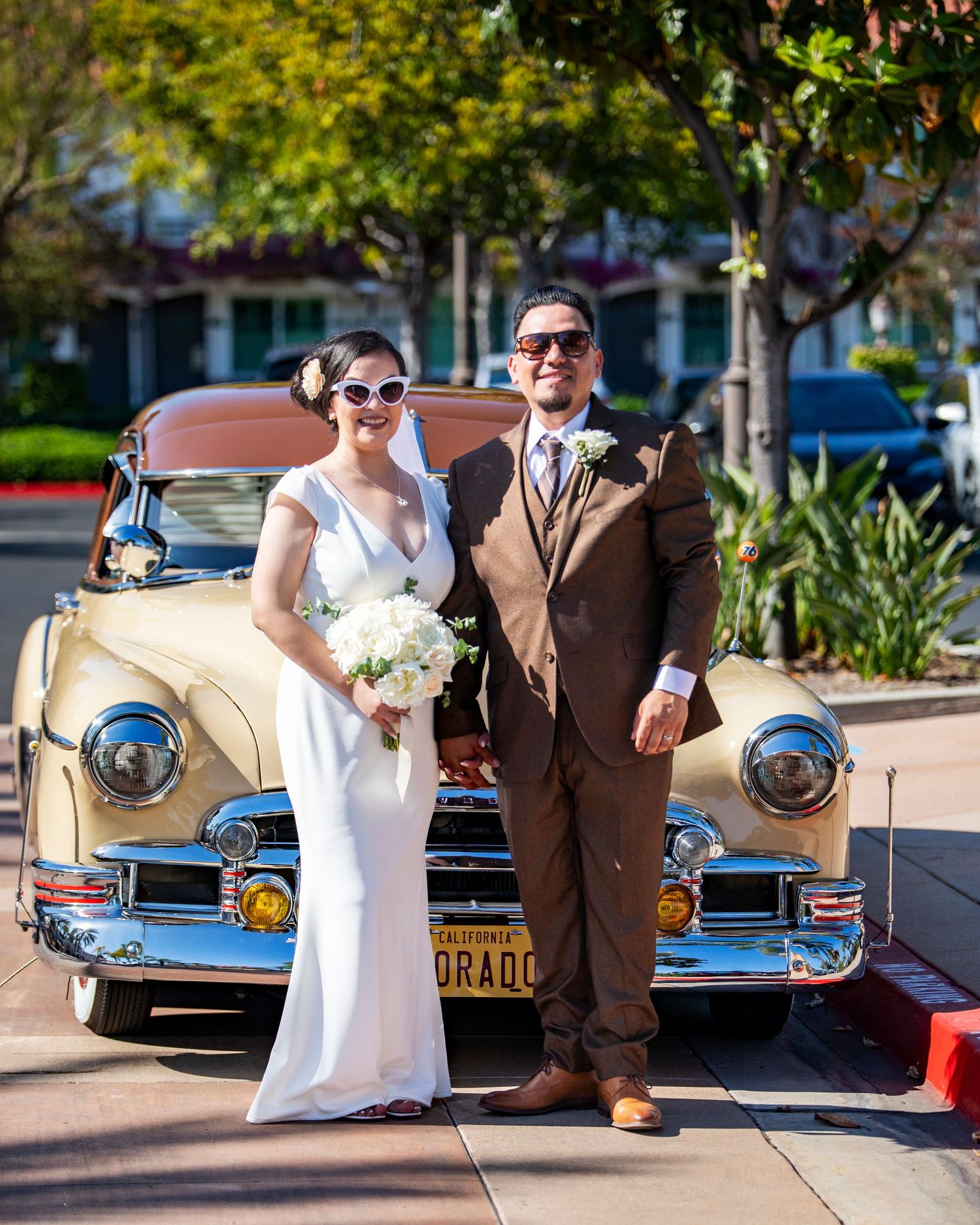 Outside the Laguna Hills Civic Center, bride and groom in retro style pose together in front of a vintage yellow classic car.