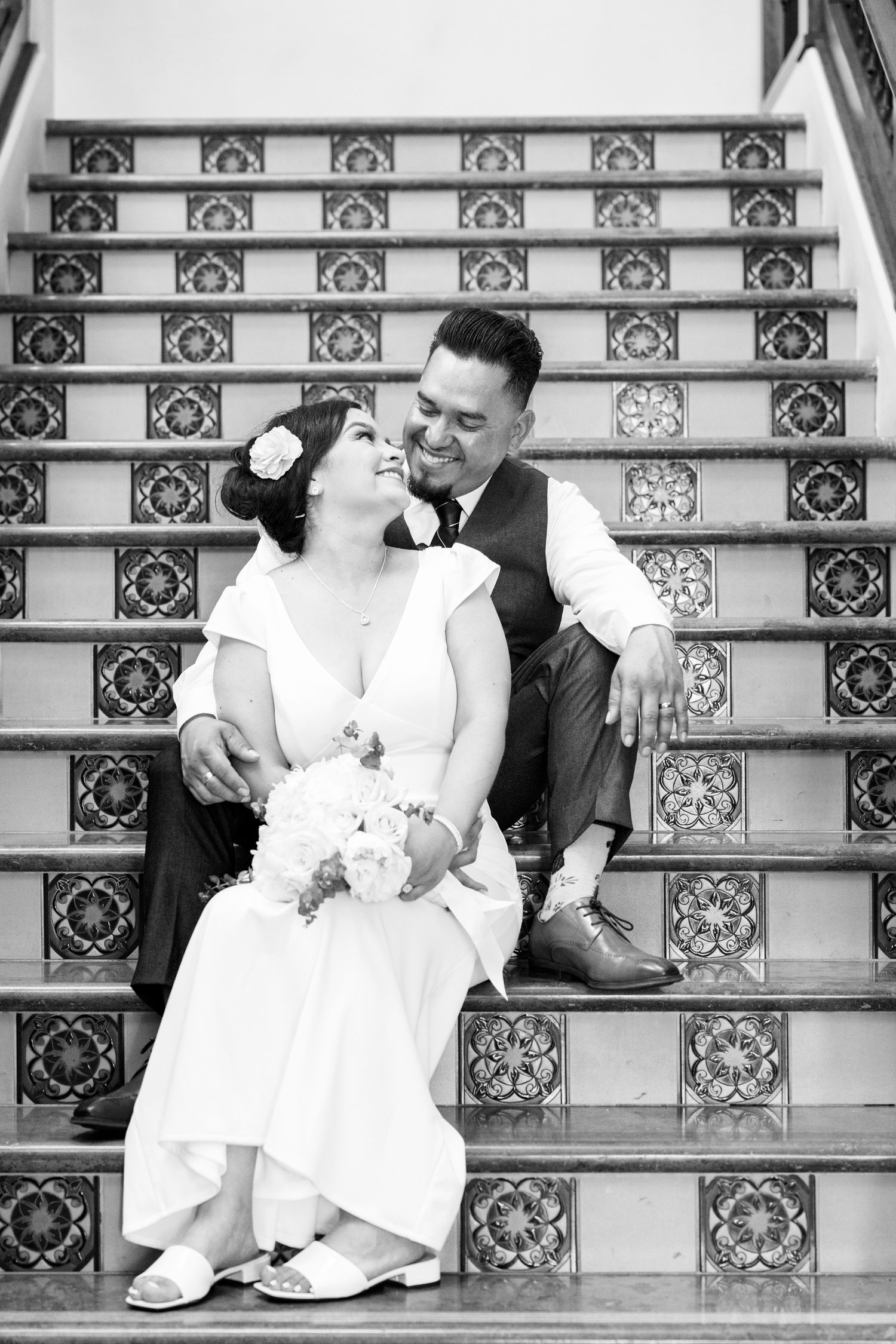 At the Laguna Hills Civic Center, wedding photos in black and white at the stairs of a bride and groom sitting and smiling.