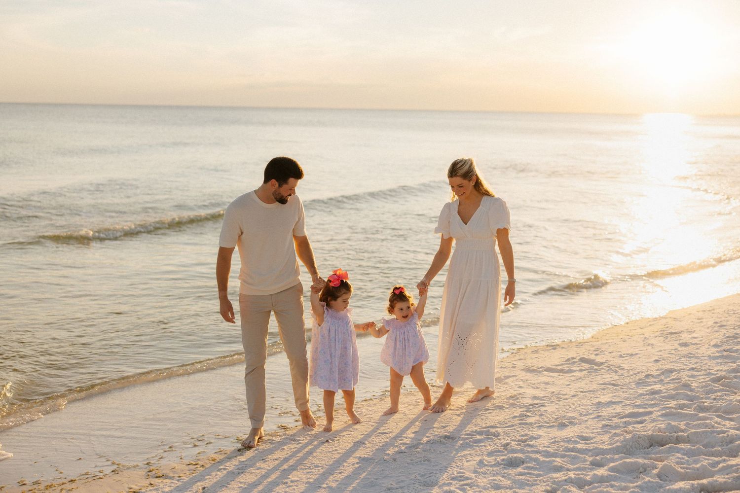 Family walks together along a sandy beach at sunset with ocean waves in the background. Santa Rosa Beach