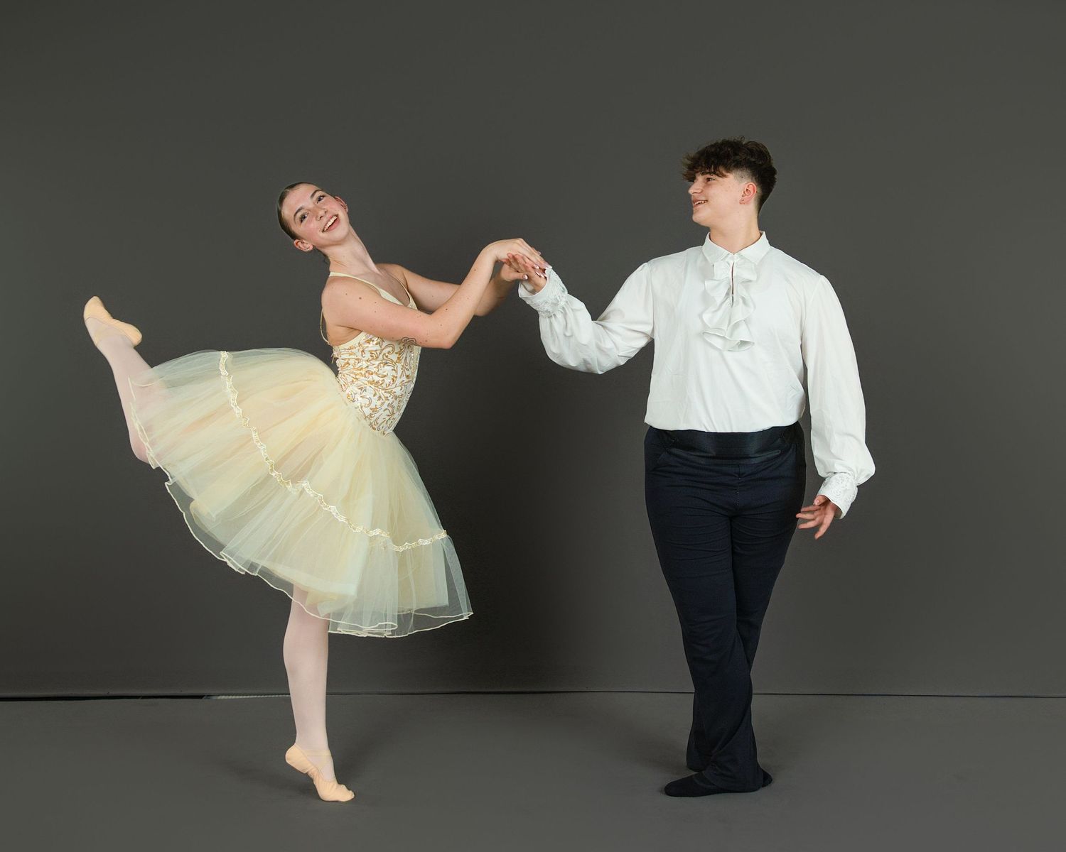 Dance partners in coordinating outfits strike a ballroom pose against a dark background.
