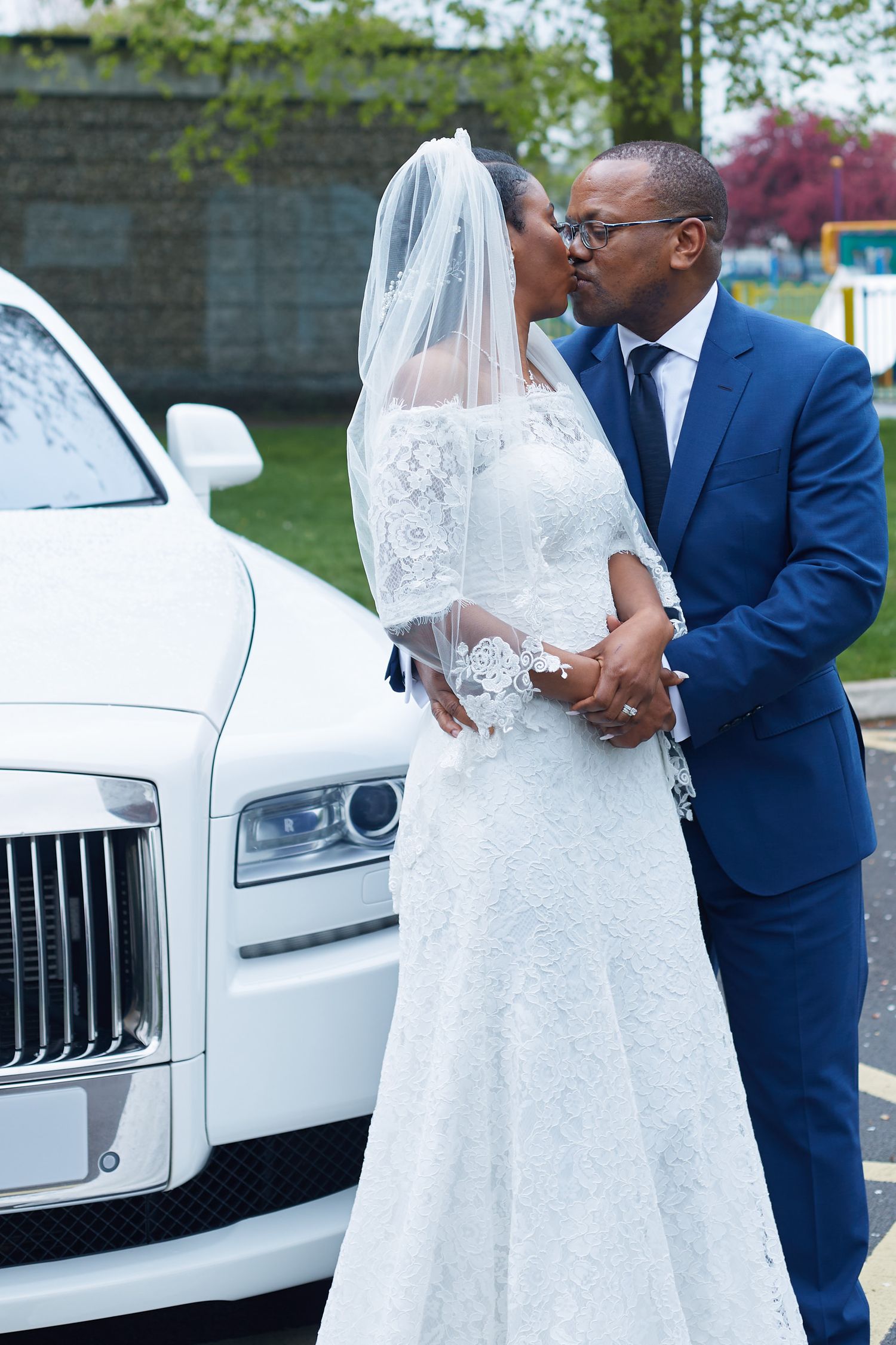 Wedding couple sharing a kiss next to a white Rolls Royce luxury car.