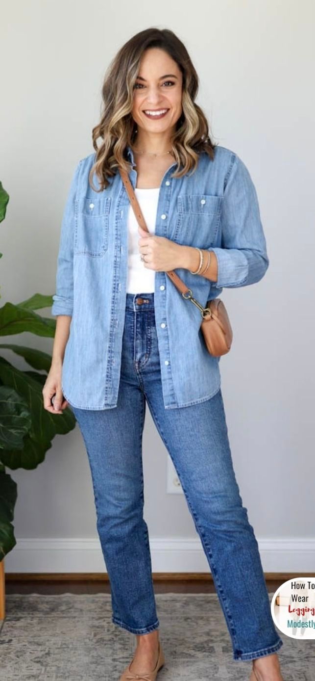 Woman wearing a chambray denim shirt over white top with straight-leg jeans and brown crossbody bag.