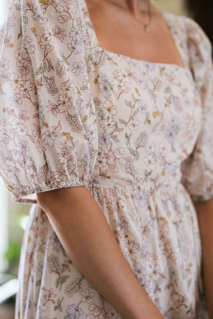 Close-up of a woman wearing a light pink floral print puff sleeve dress with a square neckline.