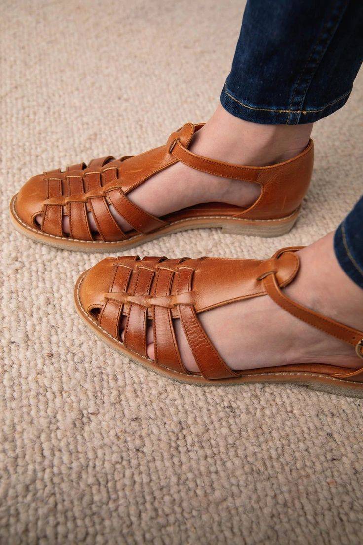 Close-up of tan brown woven leather huarache sandals worn with blue jeans on a neutral carpet.