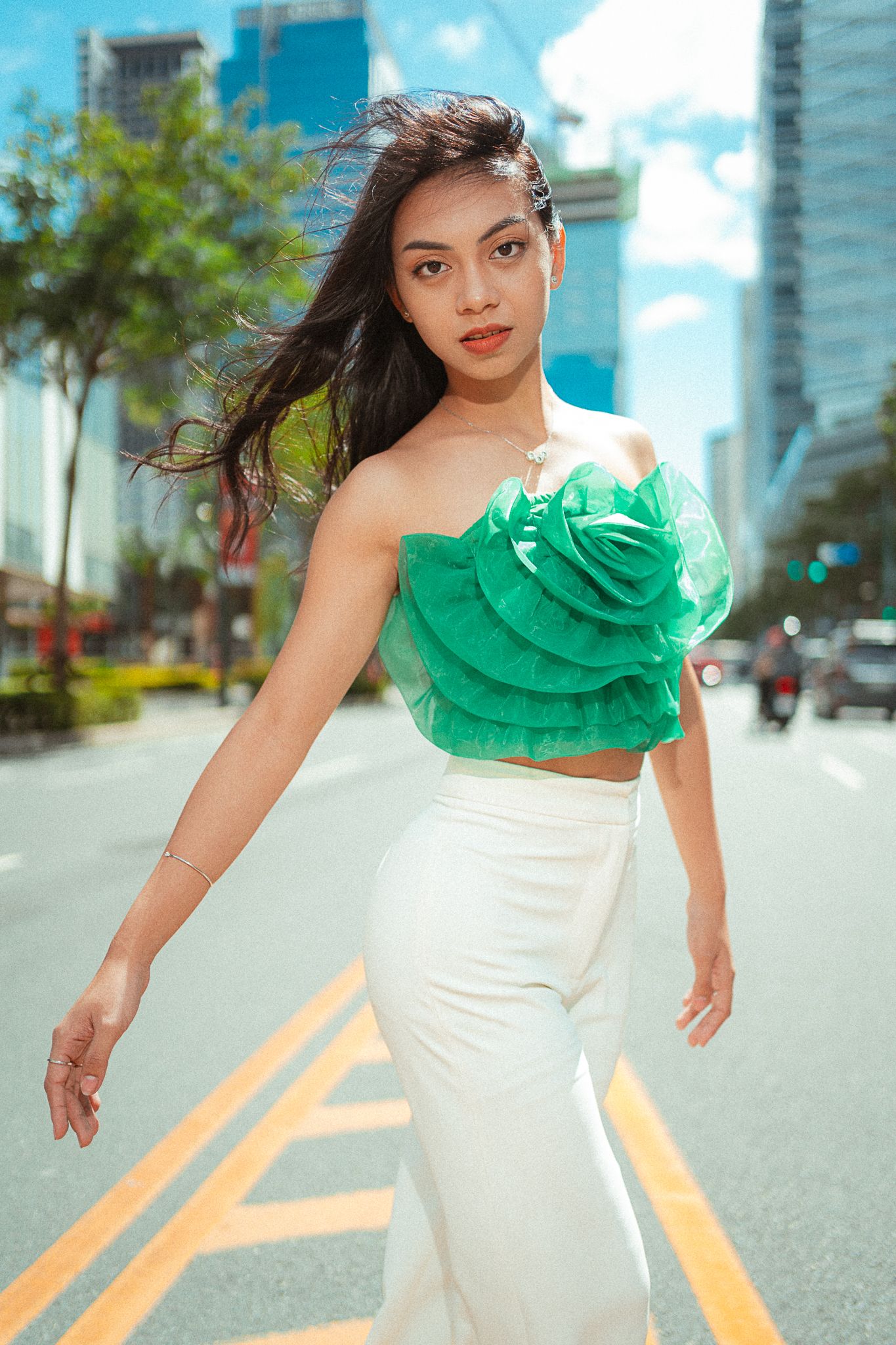 Fashion portrait of someone in an emerald green ruffled crop top and white pencil skirt on a city street with skyscrapers.