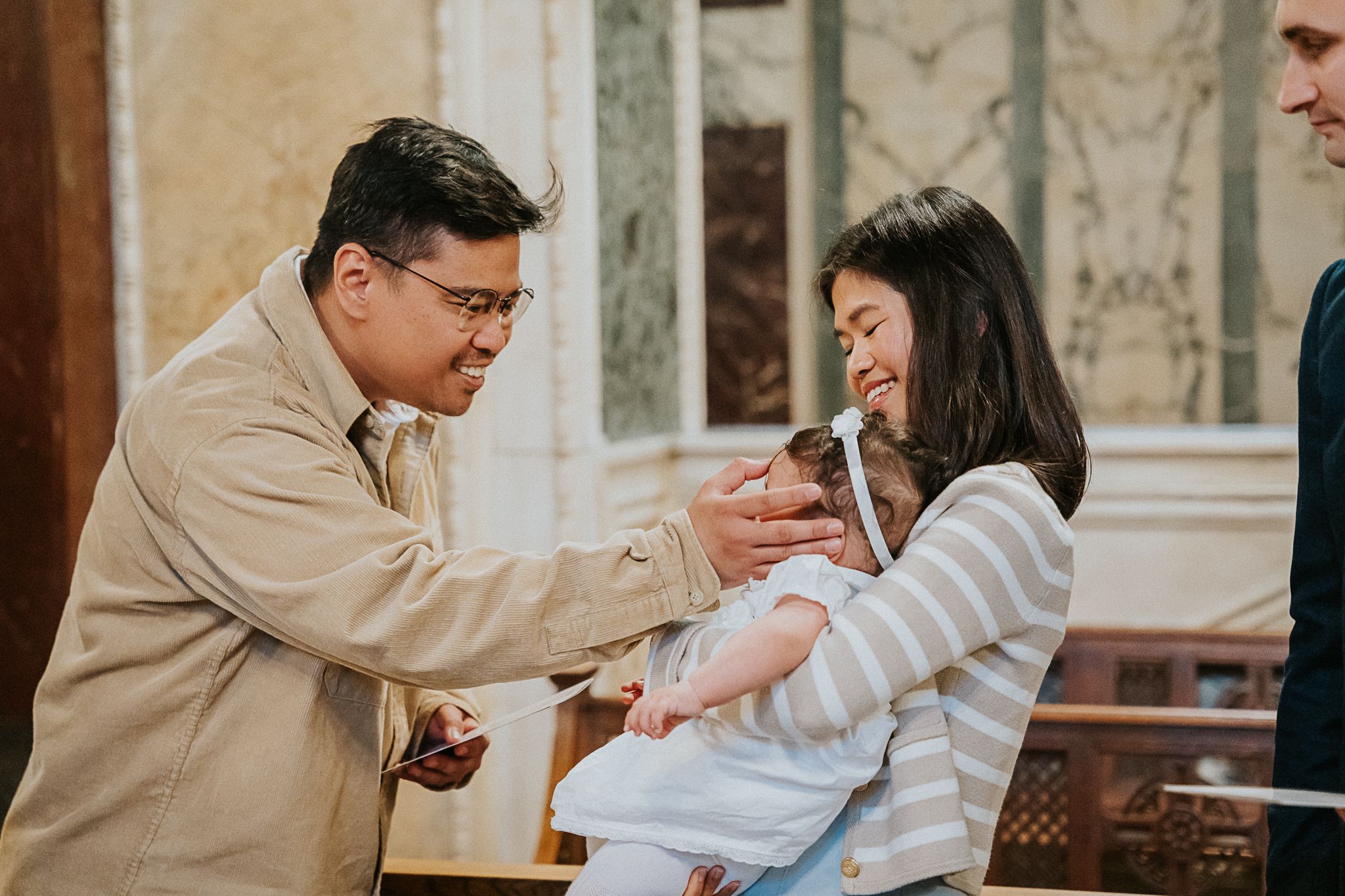A couple in tan and white sweaters lovingly gazes at their newborn baby in a warm, rustic setting.