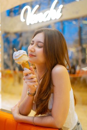 A woman in a restaurant setting takes a bite of an ice cream cone in multiple sequential photos.