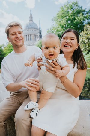 Family enjoying a sunny day together near St Paul's Cathedral in London with a baby in white outfit.