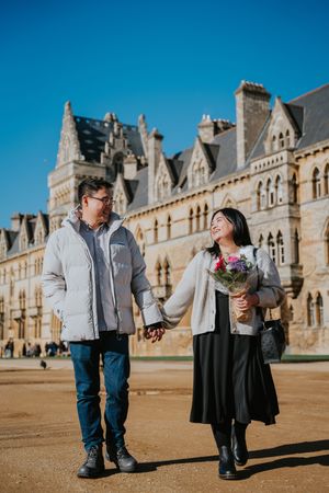 A couple shares coffee and laughter in front of ornate historic stone architecture on a sunny afternoon.