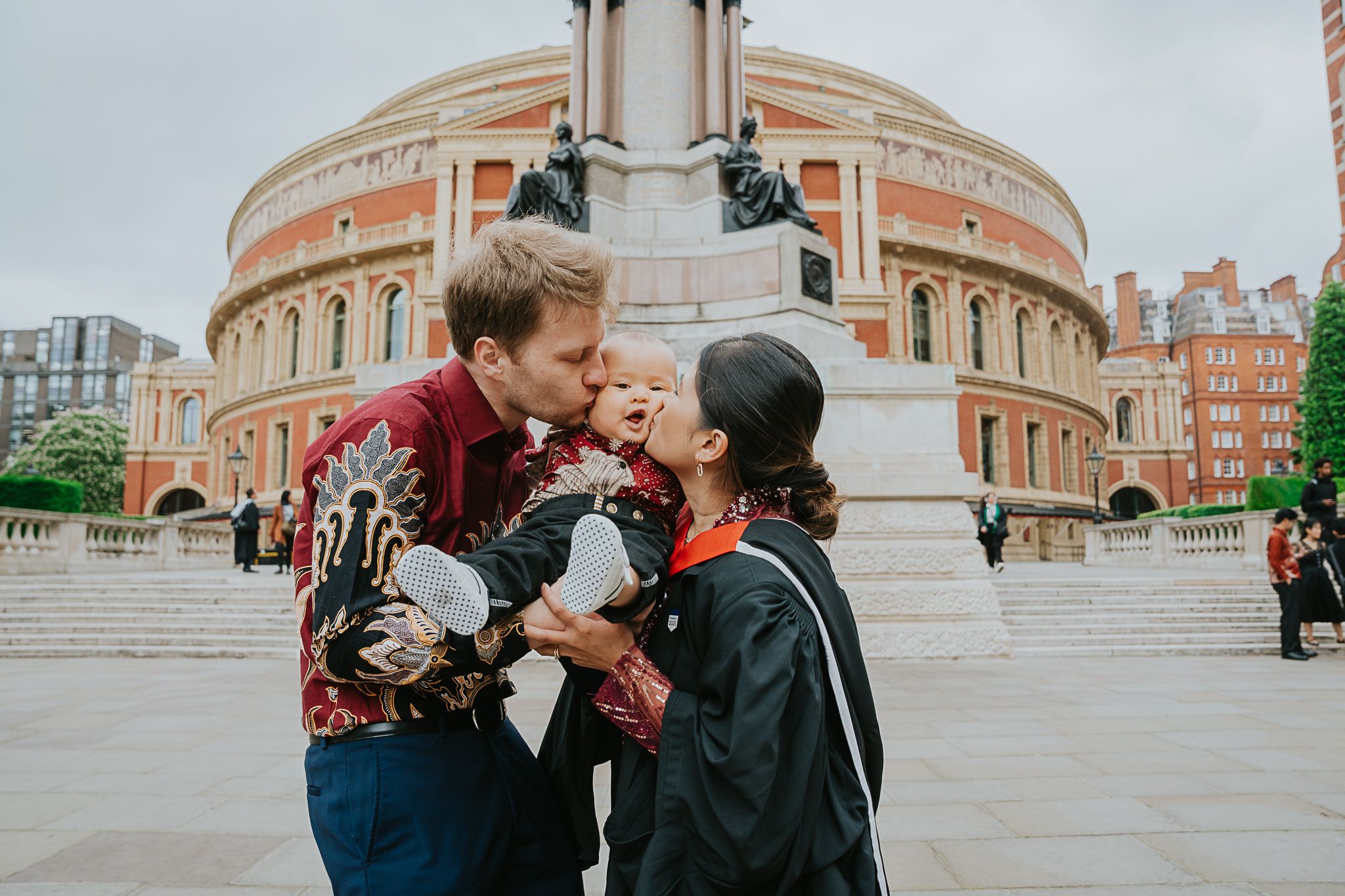 A couple shares an intimate moment outside Royal Albert Hall in London with the historic building's curved facade visible.