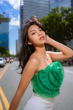A model poses in a green and white ruffle dress against urban architecture in a fashion photoshoot series.