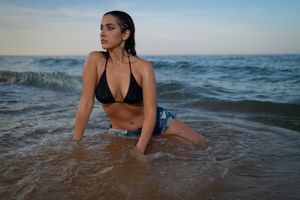 A person wades in the shimmering ocean water at sunset with waves in the background.