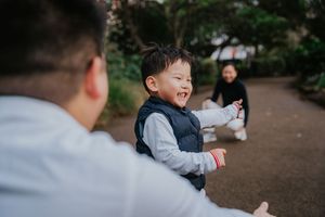A child in a gray sweater laughs while playing outdoors in a park setting during autumn.