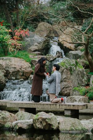 Two people enjoying serene moments by a cascading rock waterfall in a lush garden setting.