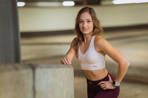 Athletic person in workout attire taking a break while leaning on concrete barrier in parking garage.