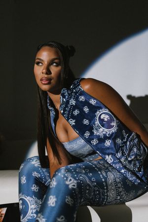 Model wearing matching blue and white bandana print activewear set crouches in dramatic lighting against white backdrop.