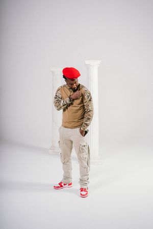 Person in red beret, tan sweater, and beige cargo pants poses in white studio setting with red sneakers.