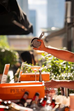 Orange Aperol Spritz being poured at an outdoor bar setting with bright summer lighting.
