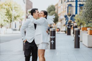Newlywed couple in white outfits sharing an intimate moment on a city street. London wedding