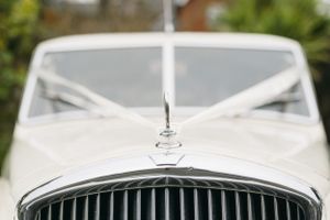 Close-up detail of a classic white Bentley car hood and grille ornament. Registry civil ceremony.