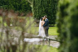 A distant view of newlyweds embracing on a path surrounded by lush greenery.
