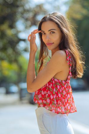 A summer portrait shows someone in a white dress with red floral ruffle detail posing outdoors in natural sunlight.