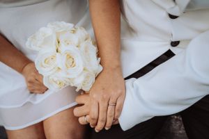 A close-up view of a couple holding hands with a white rose bouquet resting on a white dress.