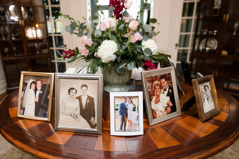 A collection of vintage family photographs displayed on a round wooden table with a floral centerpiece arrangement.