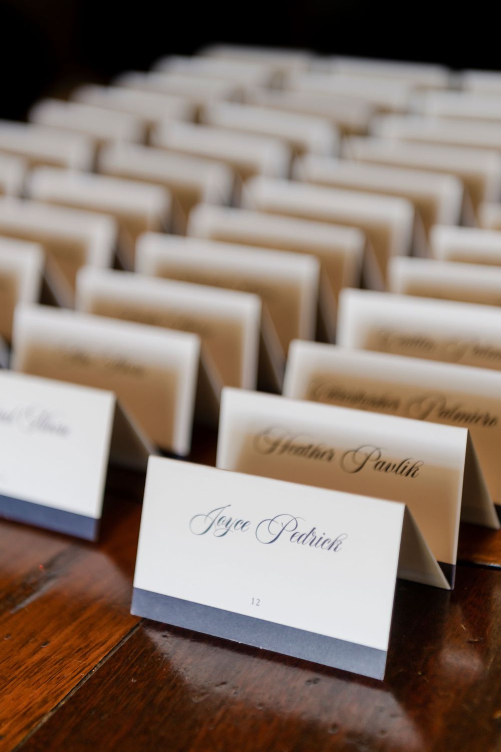 Elegant white wedding place cards with handwritten names displayed in neat rows on a dark wooden surface.