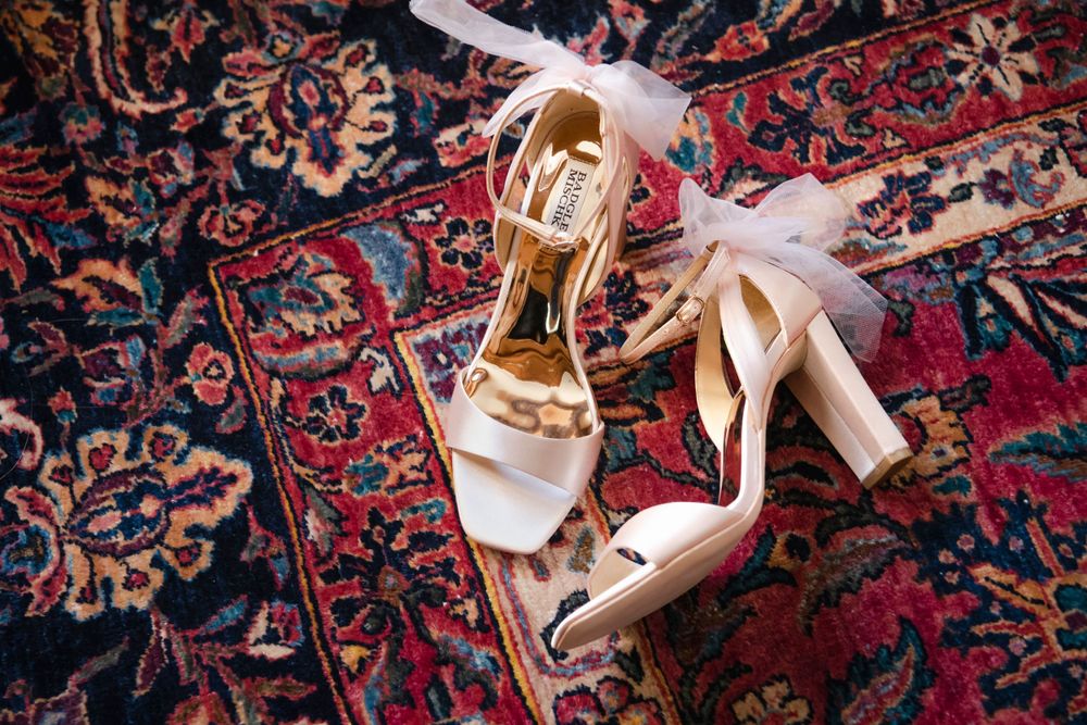 White satin bridal heels with ribbon straps displayed on an ornate red Persian rug background.
