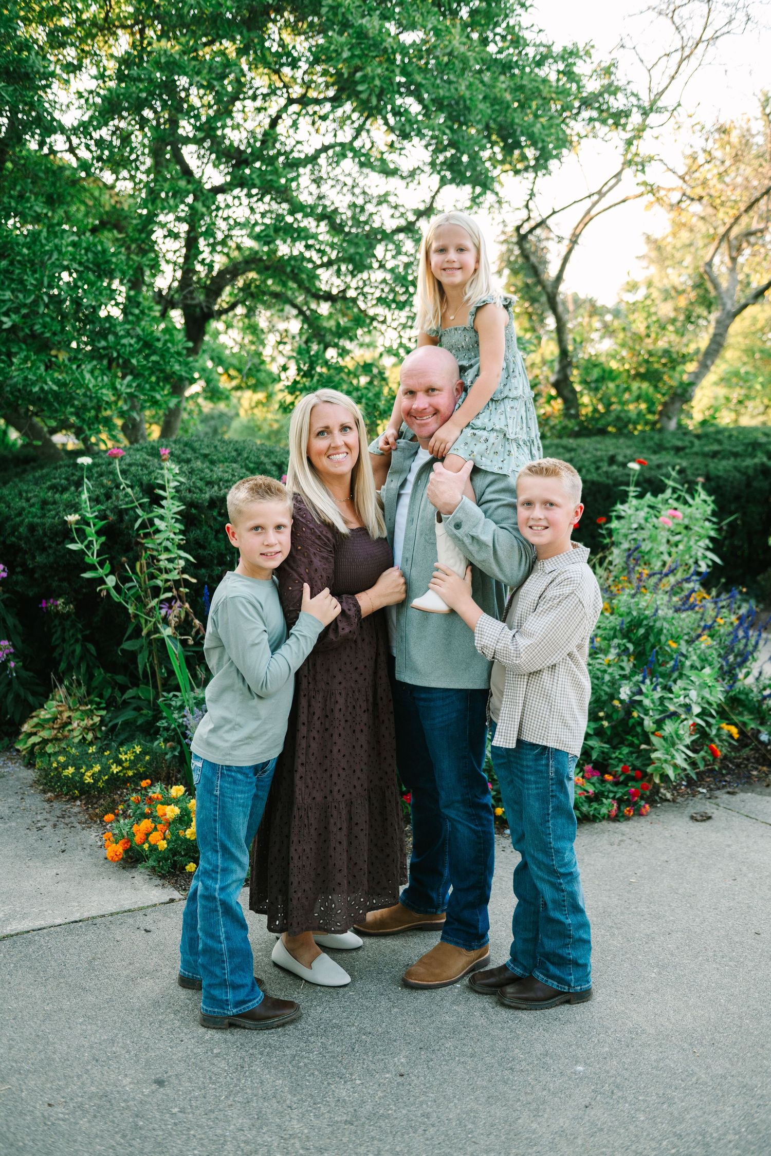 Family of five standing together on green lawn with pine trees in background.
