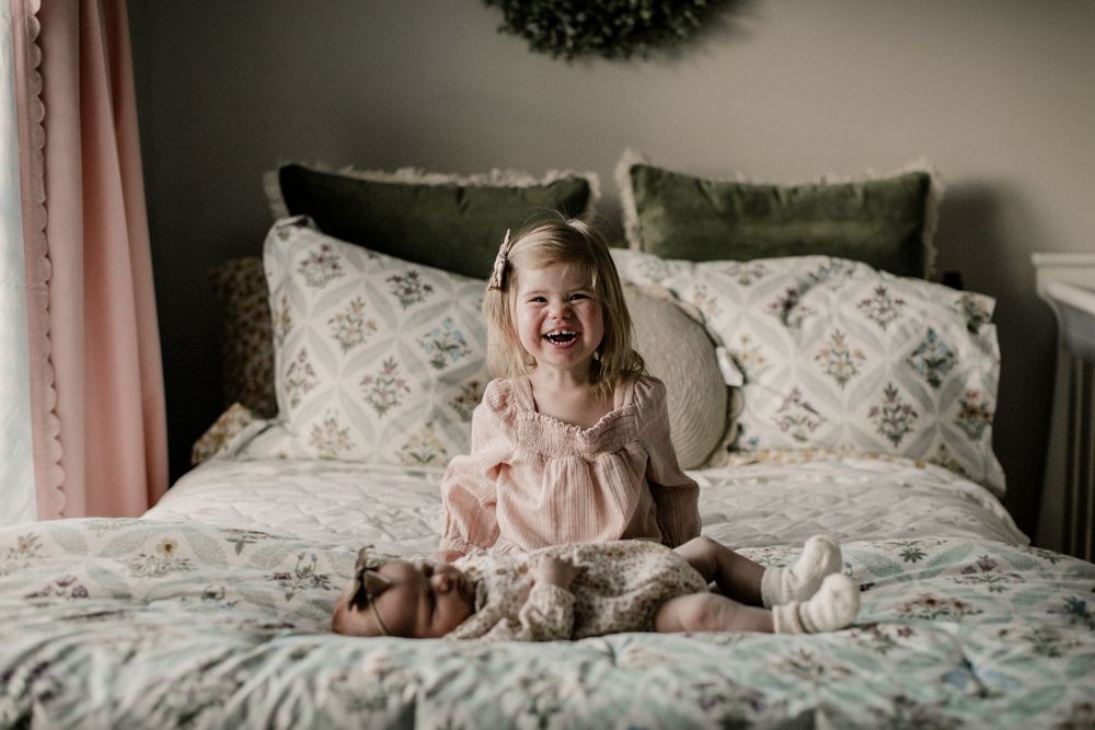 A sequence of four candid photos showing joyful moments on a bed with white floral bedding and pink walls.