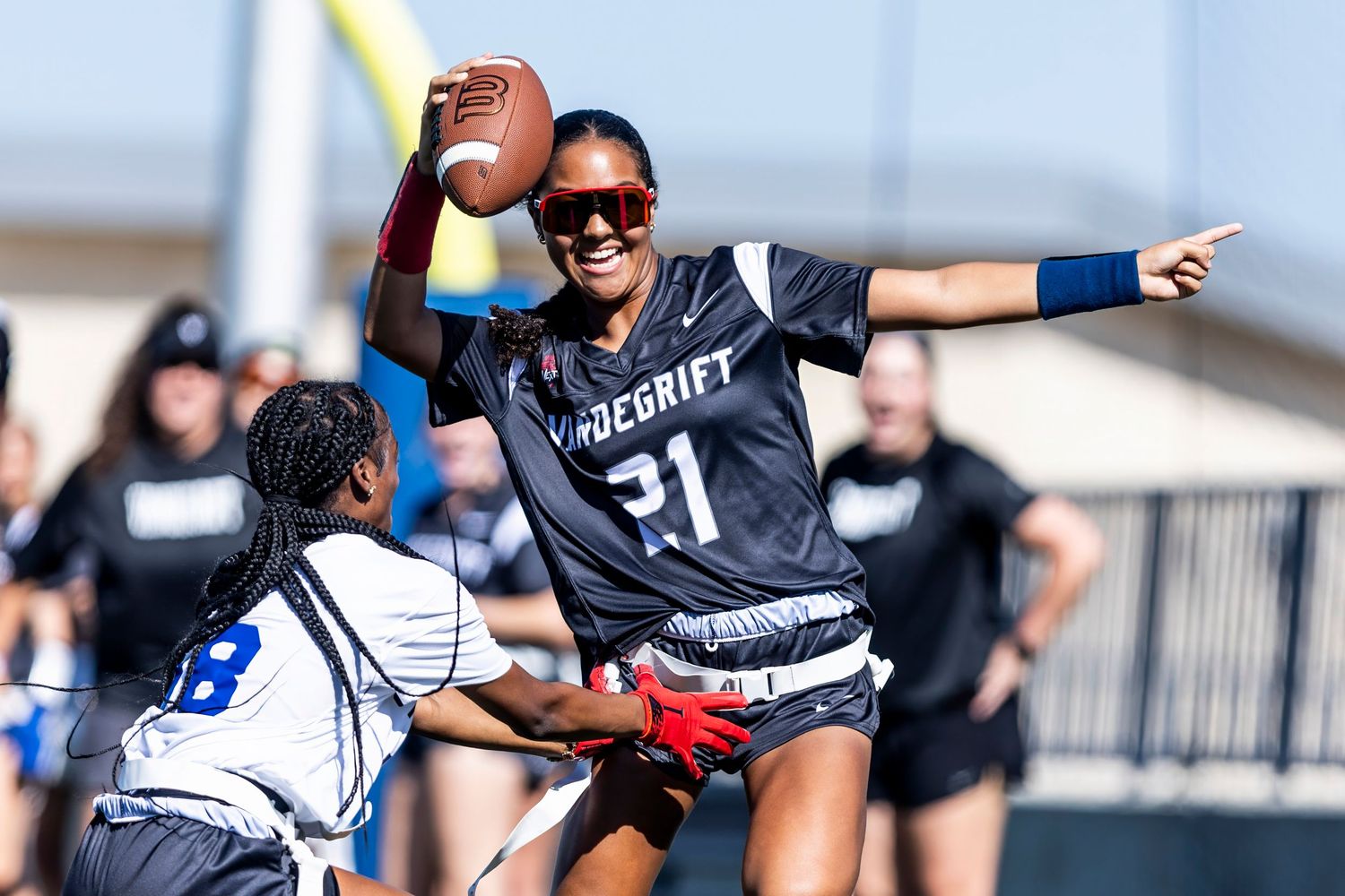 Female flag football player in Vandegrift jersey #21 catches pass during competitive outdoor game.